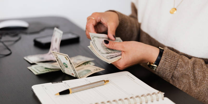 A Woman Counting Money on a Black Desk for Her Long-term Care Premium Deduction 2022 With Corona Estate Planning Attorney